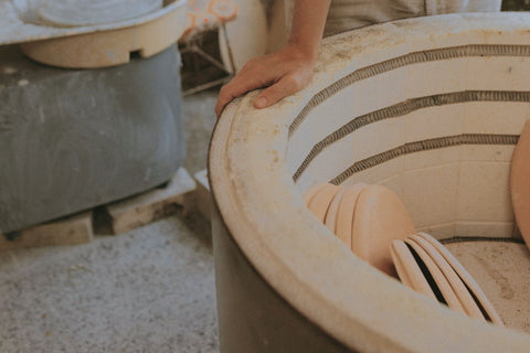 hand resting on the exterior of a pottery kiln with a few shelves inside