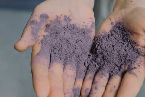 hands gently holding a small pile of purple ceramic pigment powder